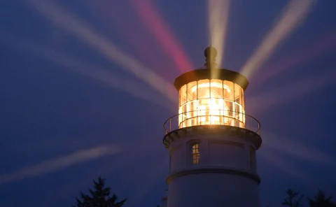 A lighthouse beaming rays of light into dark evening sky