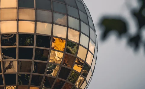 Close-up of a reflective glass dome building at sunset, with golden light and tree leaves framing the modern architectural design